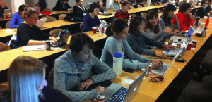 Participants actively learning software while sitting next to each other with their computers at long tables.