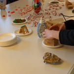 A student constructing her graham cracker gingerbread house surrounded by peppermints and other candy for decoration.