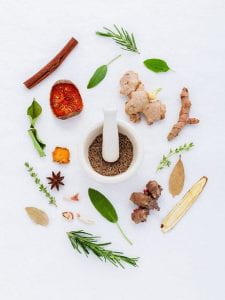 A variety of herbs decoratively placed around a mortar and pestle.