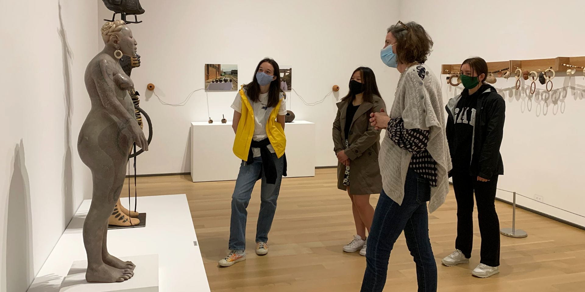A group of college-aged students on a tour with a museum educator. They are in a white gallery and looking at contemporary Native American ceramic art.