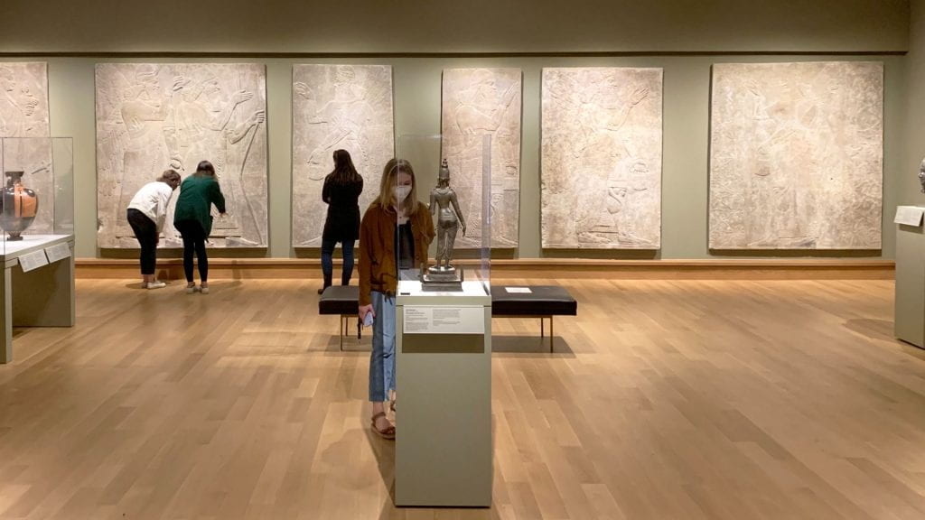 Four college-aged students look at works of ancient art in a museum gallery.