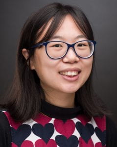 A portrait photograph of a young Asian woman with short dark hair and wearing round glasses.