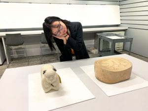 A young woman rests her head on her hands as if they were a pillow while looking at two ancient Chinese ceramic pillows.
