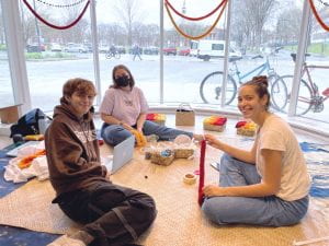 Three students sit in a circle and make yarn leis.