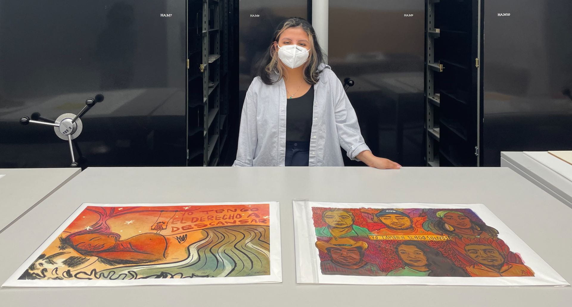 A person in their 20s standing behind a table with two prints made by a Mexican artist.