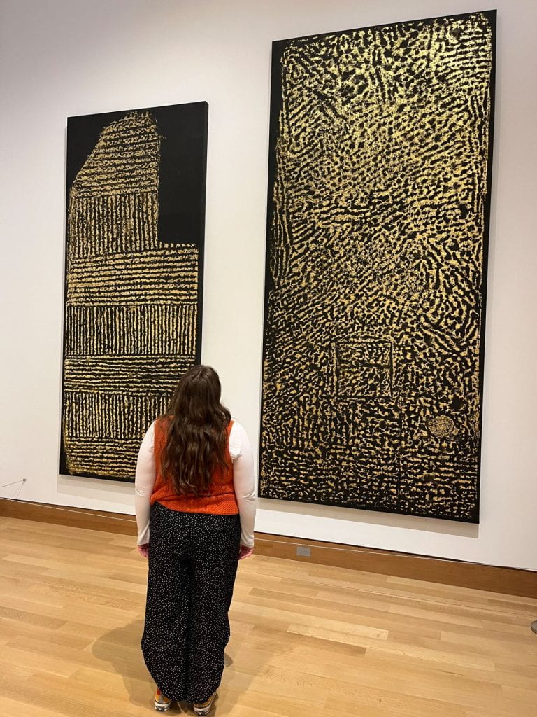 Lathrop Gallery with black and gold vertical works by James Nares titled Greenwich I (2018) and Lafayette VII (2019). The black background emphasizes the textured gold accents, inviting viewers to contemplate the connection to fashion