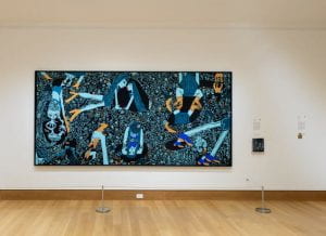 "Blue Puddles" (2021) by Summer Wheat is displayed in Jaffe Gallery. The artist achieved a 3D effect by pressing paint through aluminum mesh, creating a bubbling, textured illusion reminiscent of embroidery. Though not embroidered, the artwork's appearance may deceive. Nearby, a touch component allows tactile exploration of the piece.